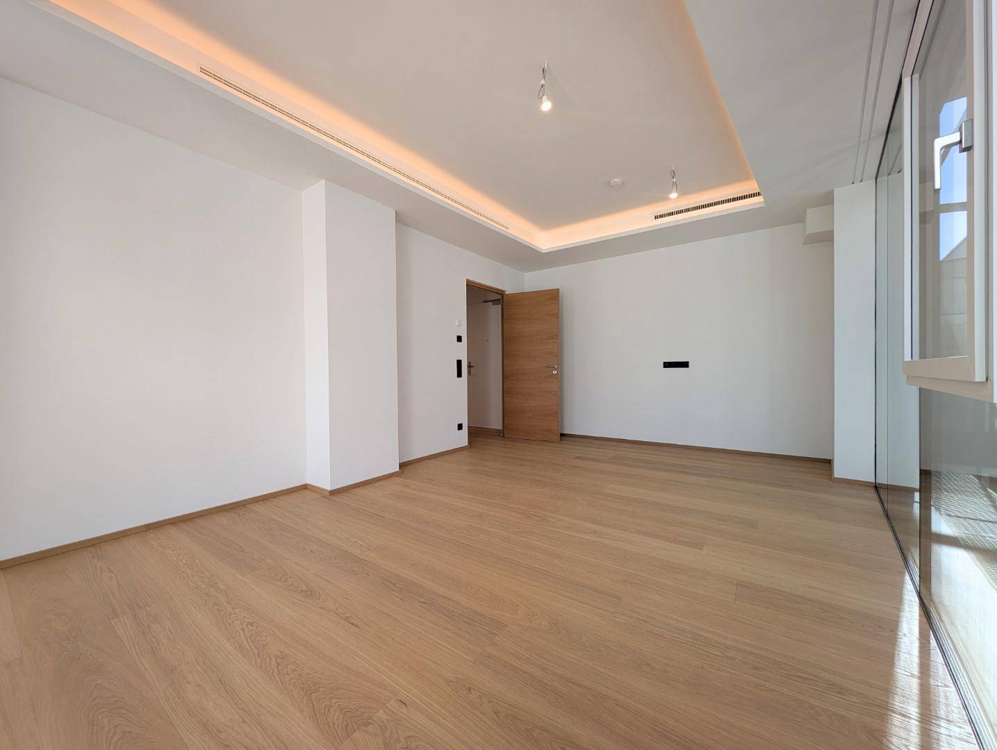 Geräumiges Schlafzimmer mit Holzboden, indirekter Deckenbeleuchtung und großen Fenstern.
