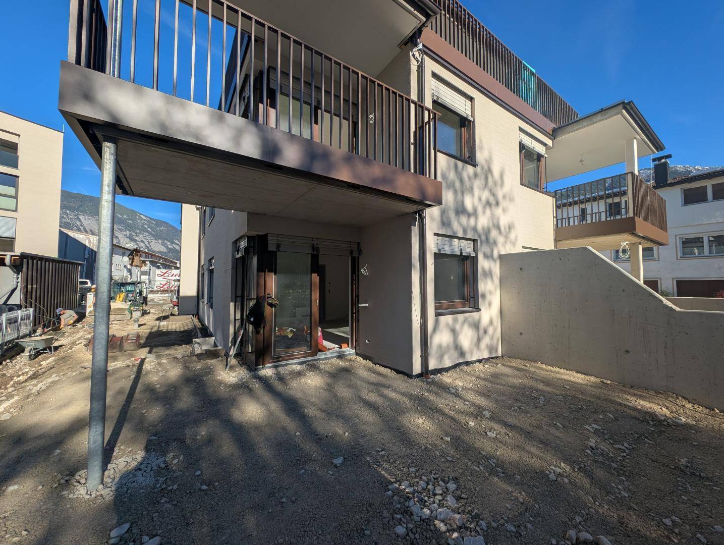 Seitenansicht des im Bau befindlichen Gebäudes mit Balkon und Zugang zum Außenbereich.