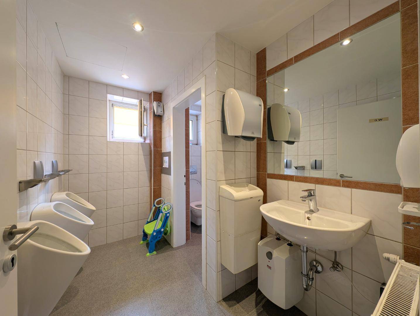 Geräumiges Badezimmer mit Waschbecken, Spiegel und mehreren Urinalen.