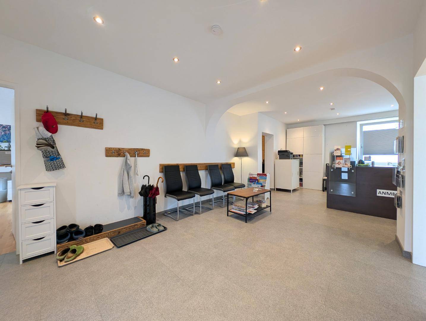 Heller Empfangsbereich mit Sitzgelegenheiten, Garderobe und einem Rezeptionstresen.