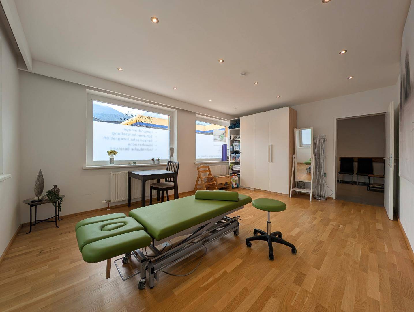 Heller Therapieraum mit Holzboden, grüner Behandlungsliege und praktischen Schränken.