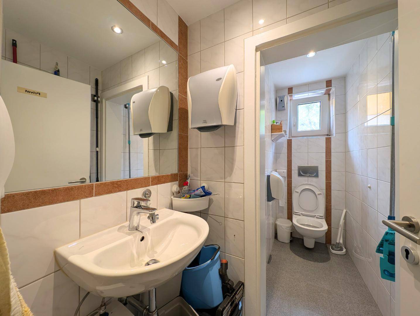 Badezimmer mit Waschbecken, Spiegel und Toilette, hell gefliest.