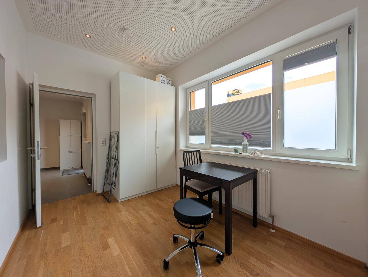 Büro mit Holzboden, weißem Schrank und großem Fenster mit Sichtschutz.