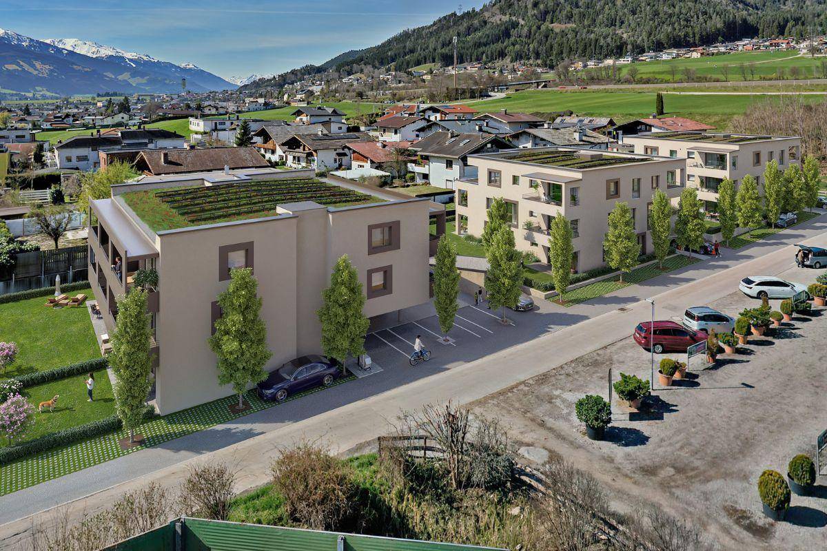 Moderne Wohnanlage mit Tiefgaragenzufahrt und Außenstellplätzen vor alpiner Bergkulisse.