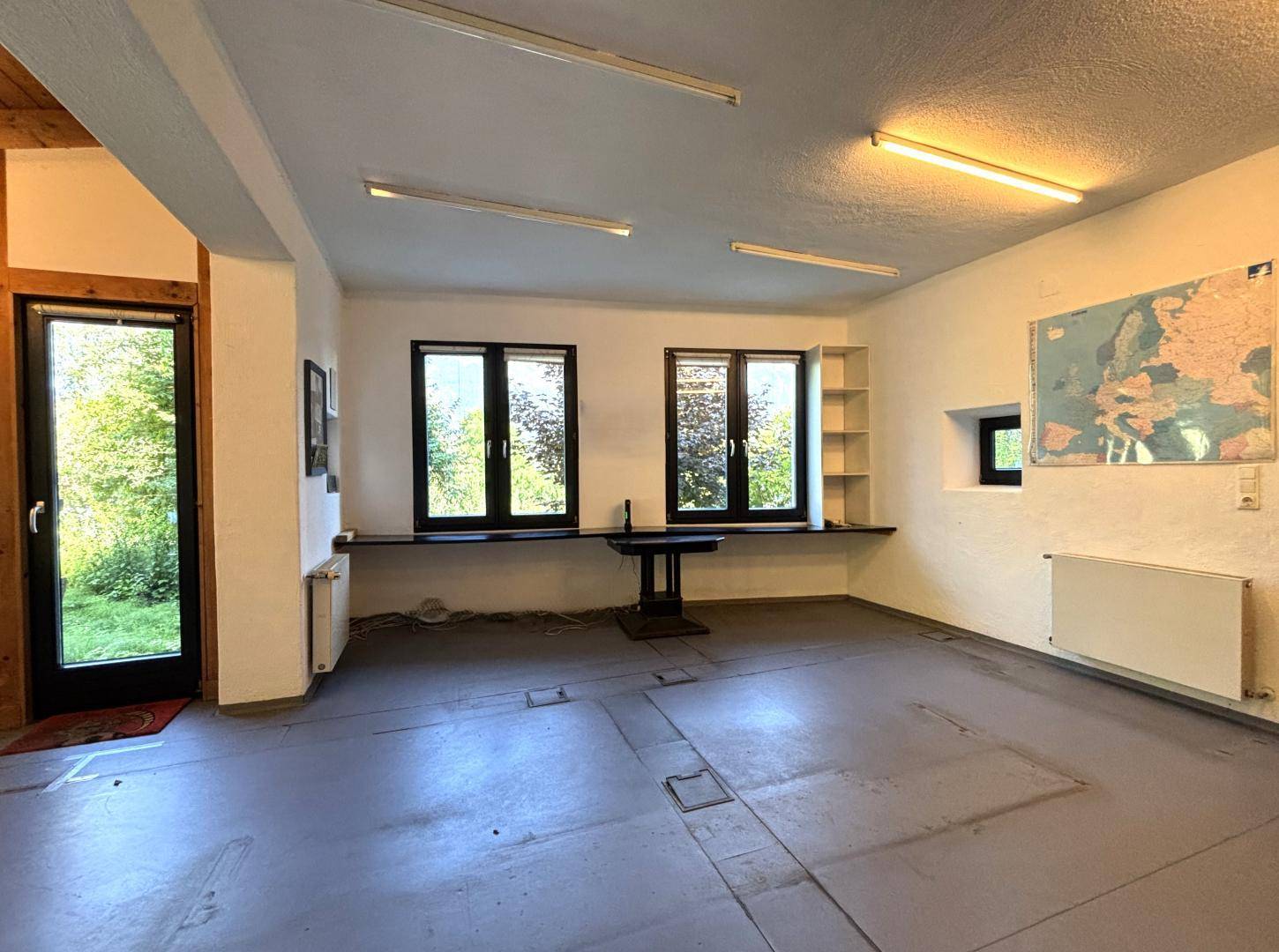 Heller Raum mit weißen Wänden, großen Fenstern und einem Weltkartenposter an der Wand.