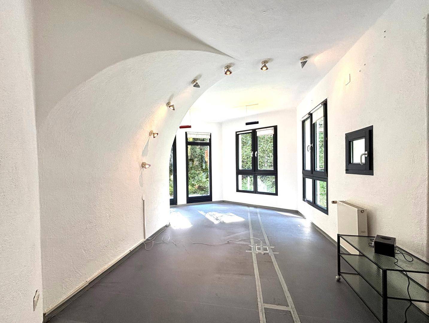Moderner Raum mit geschwungener Wand, vielen Fenstern und Deckenstrahlern.