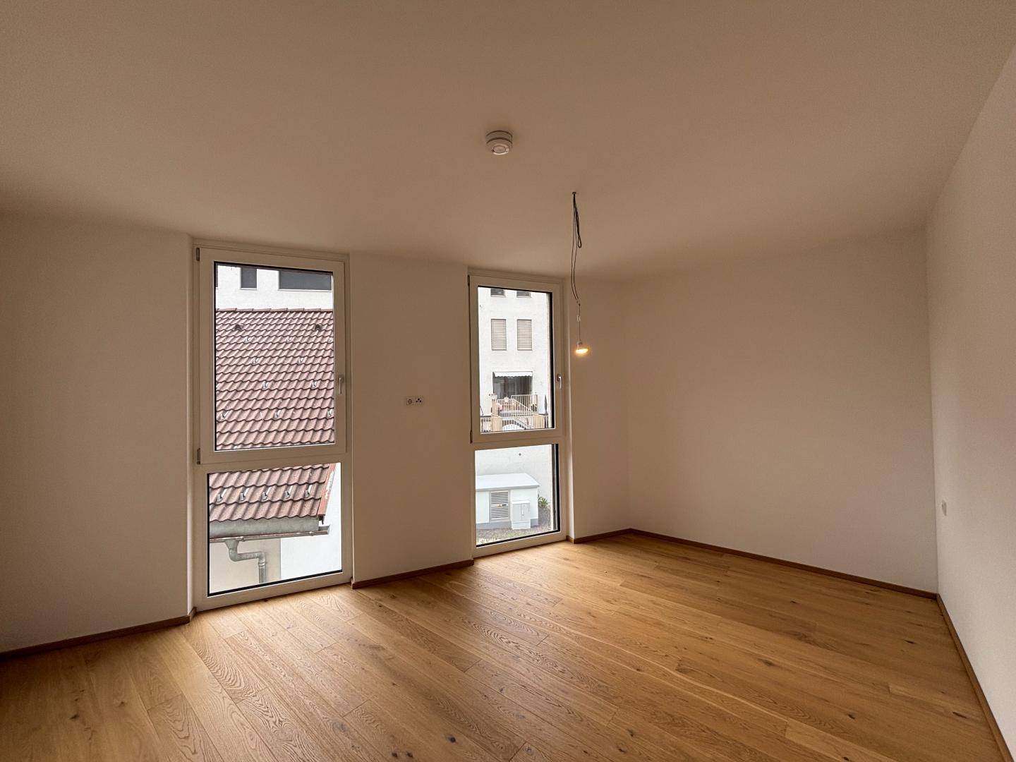 Helles Zimmer mit Holzparkettboden und zwei hohen Fenstern, bereit zur individuellen Gestaltung.