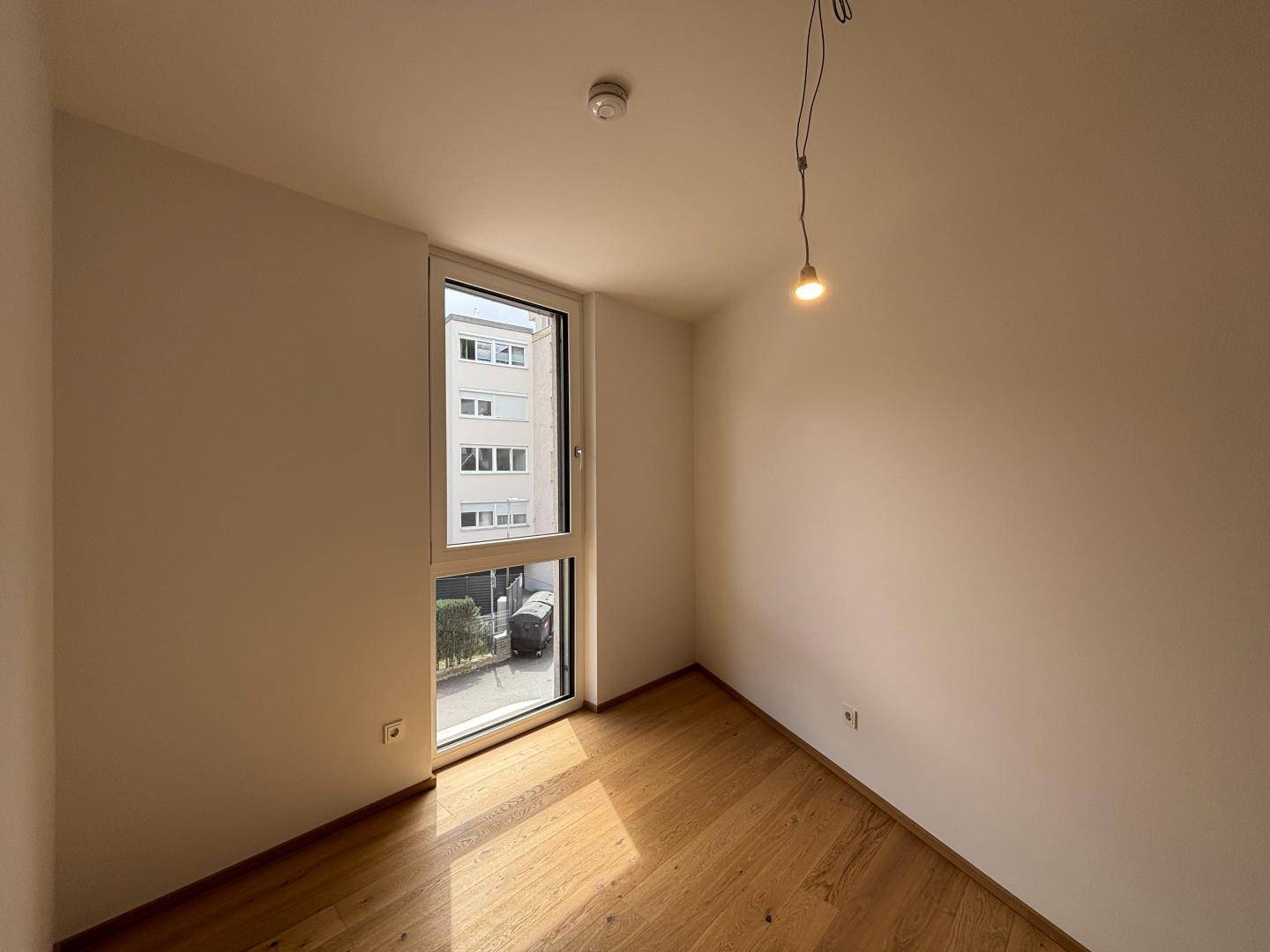 Kleineres Zimmer mit Holzparkett und einem hohen Fenster, ideal als Kinder- oder Arbeitszimmer.