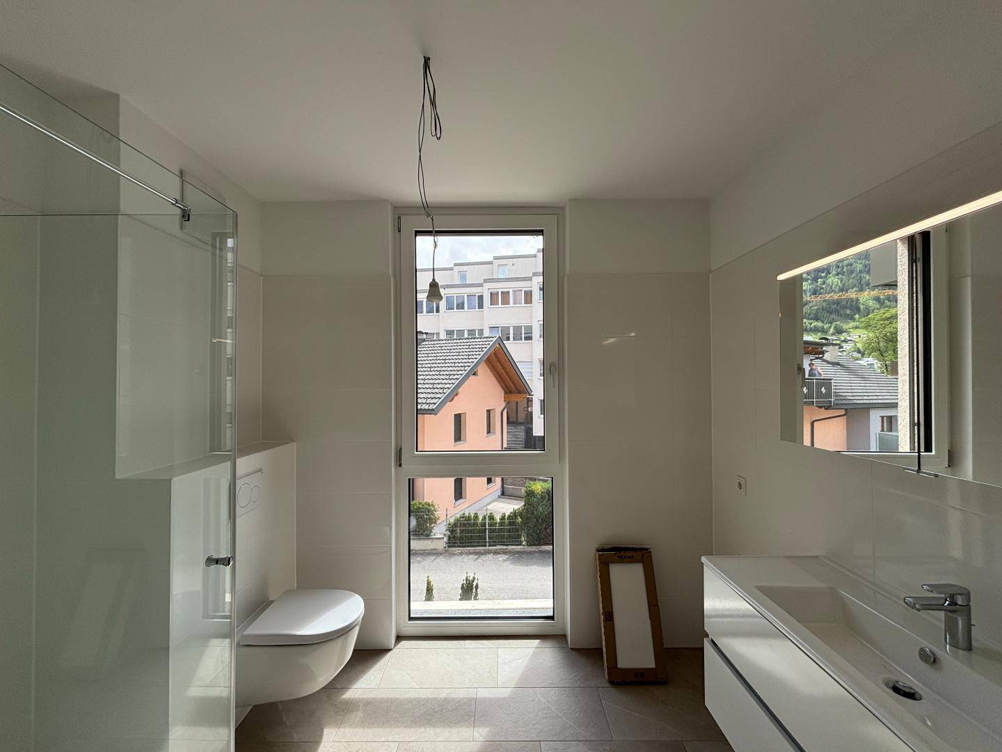 Modernes Badezimmer mit großformatigen Fliesen, wandhängendem WC und Fenster.
