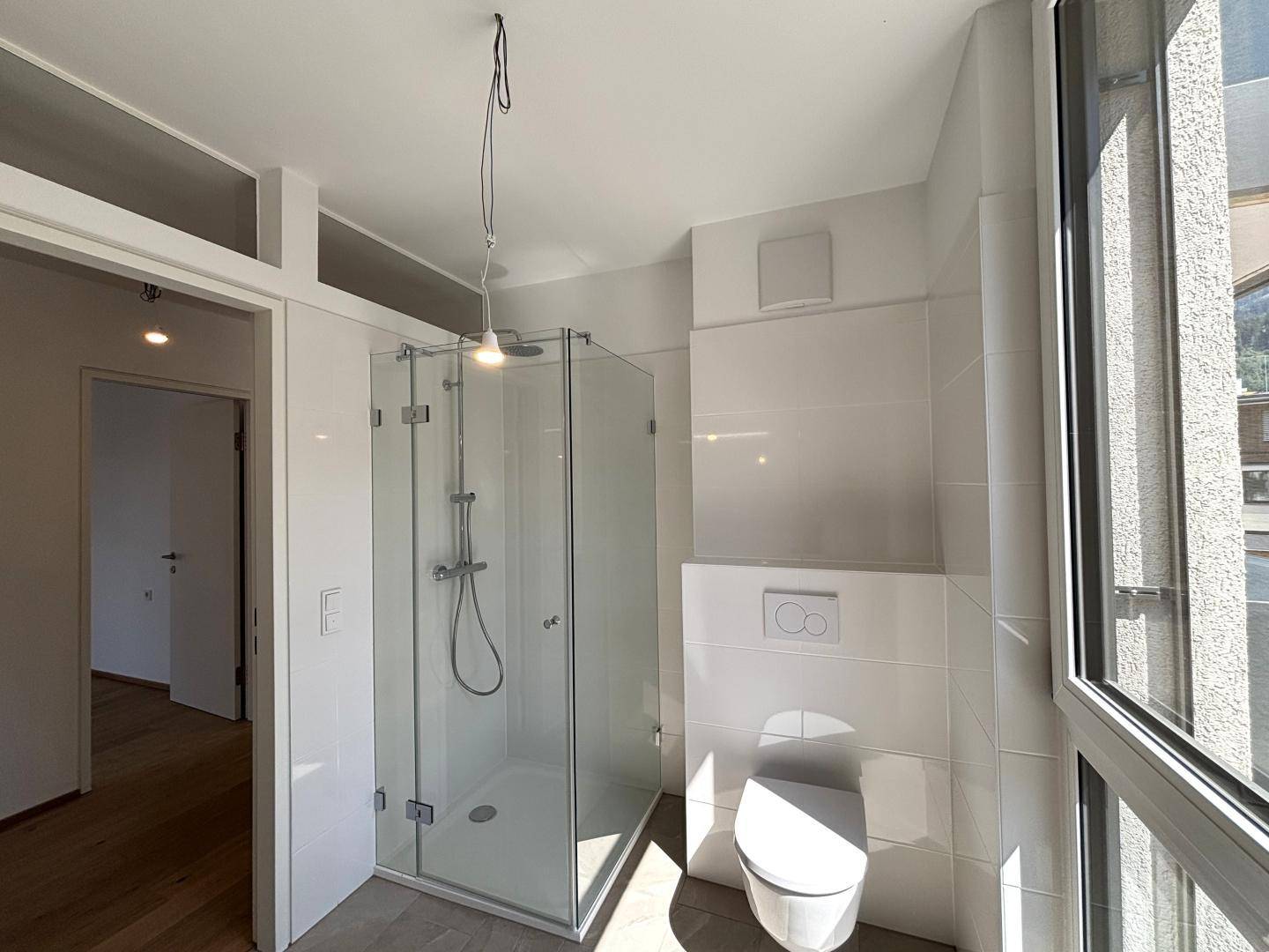 Helles Badezimmer mit begehbarer Dusche, wandhängendem WC und großem Fenster.
