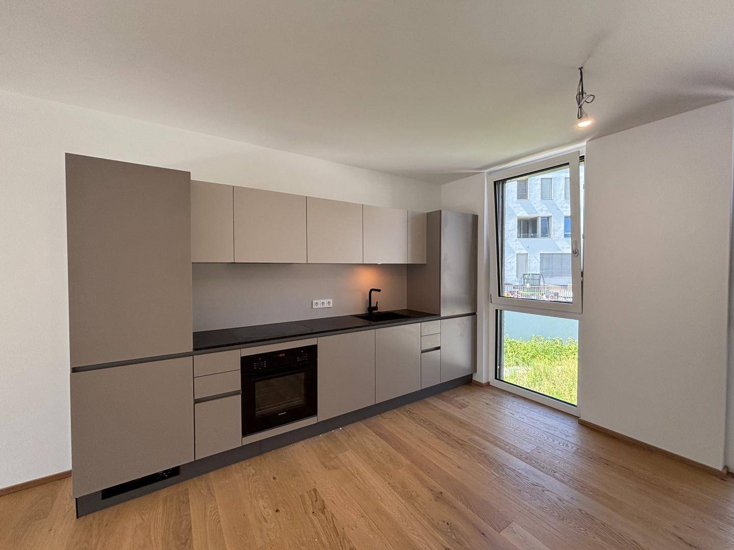 Moderne Küchenzeile mit integrierten Geräten, Holzboden und großem Fenster für viel Tageslicht.