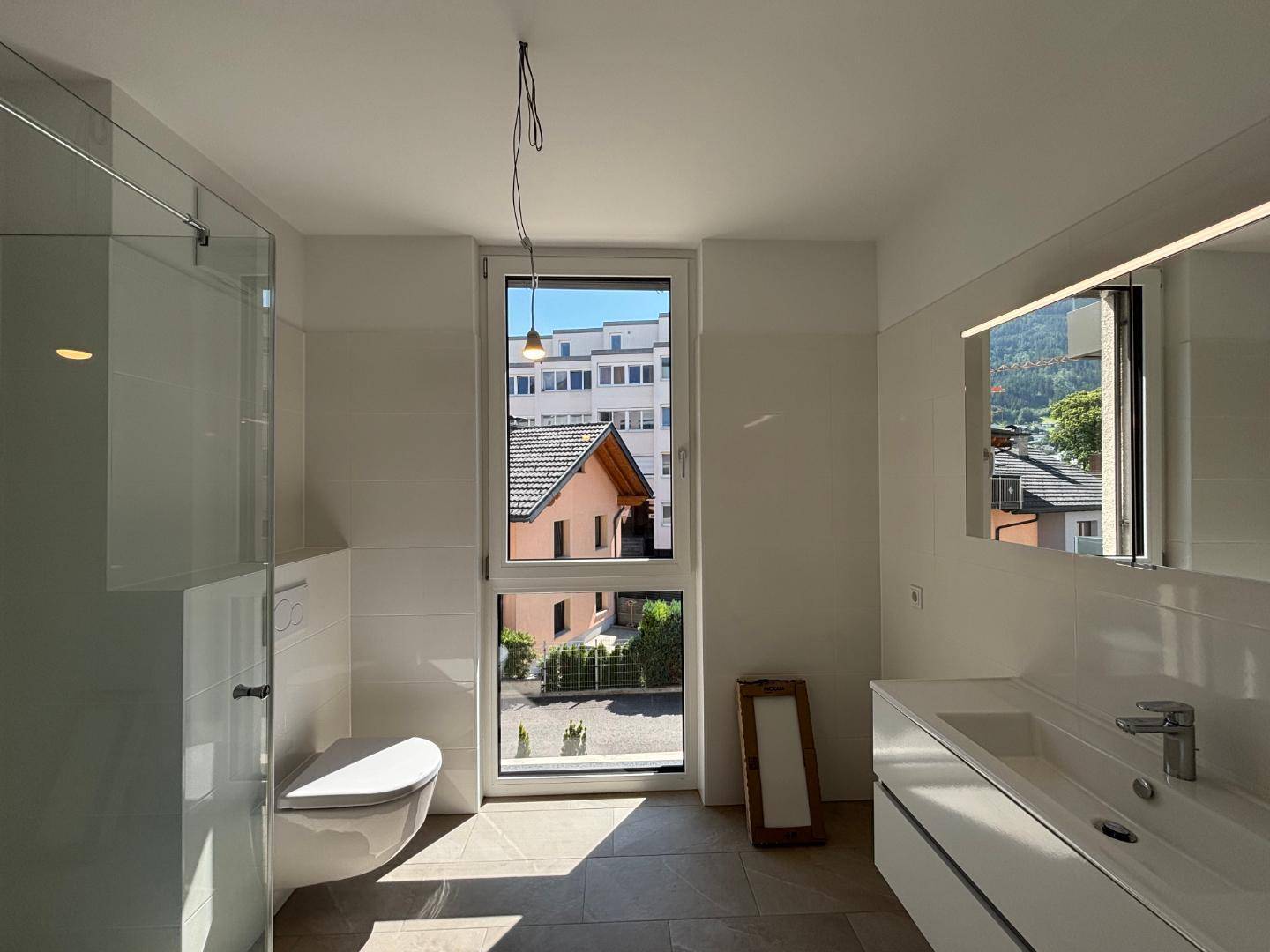Helles Badezimmer mit modernem Waschtisch, Spiegel und Fenster mit Blick ins Grüne.