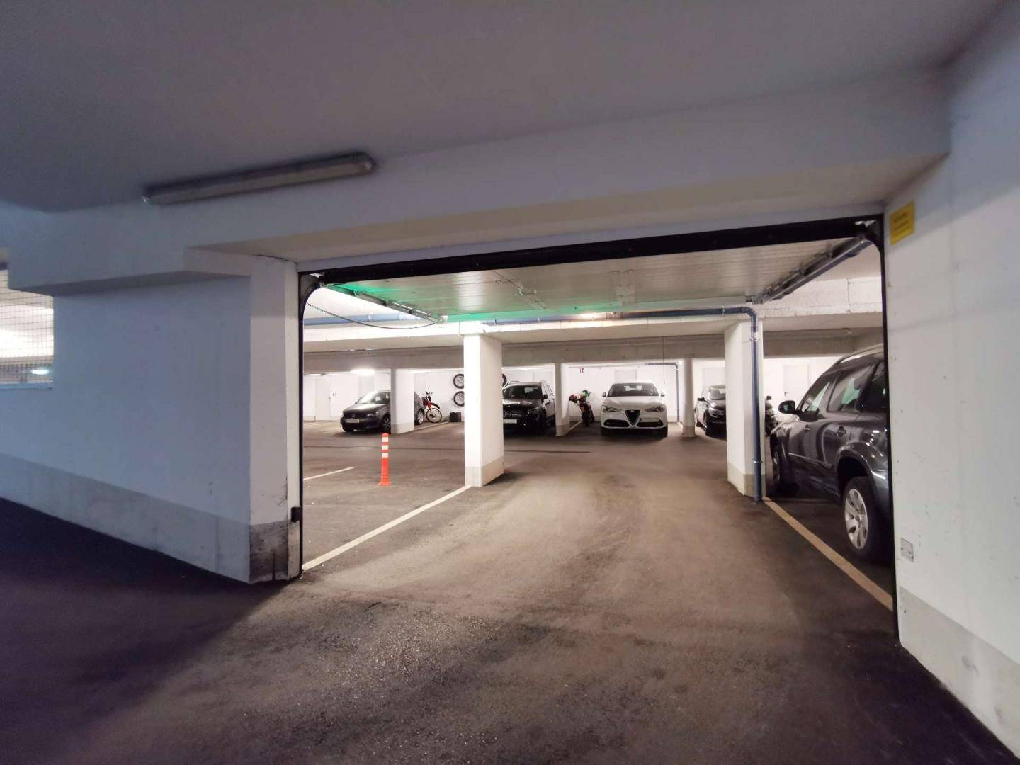 Blick in die moderne Tiefgarage mit mehreren geparkten Fahrzeugen und breiter Zufahrt.