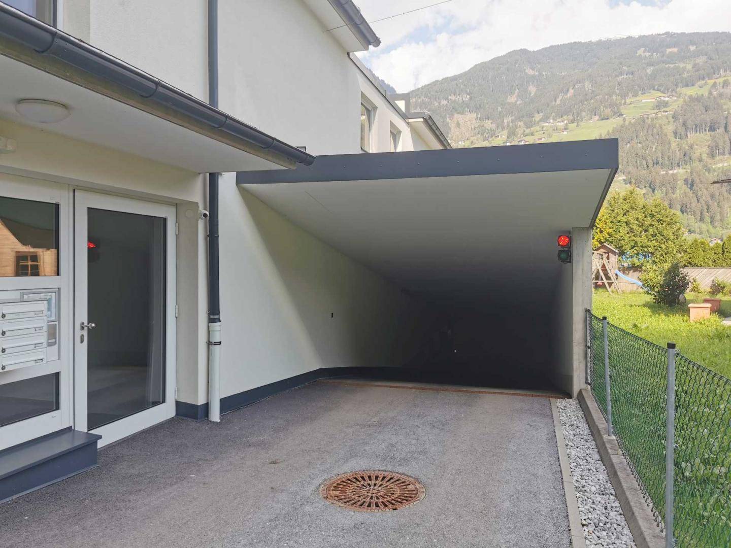 Eingang zur Tiefgarage eines modernen Gebäudes mit Bergblick und gepflegter Außenanlage.