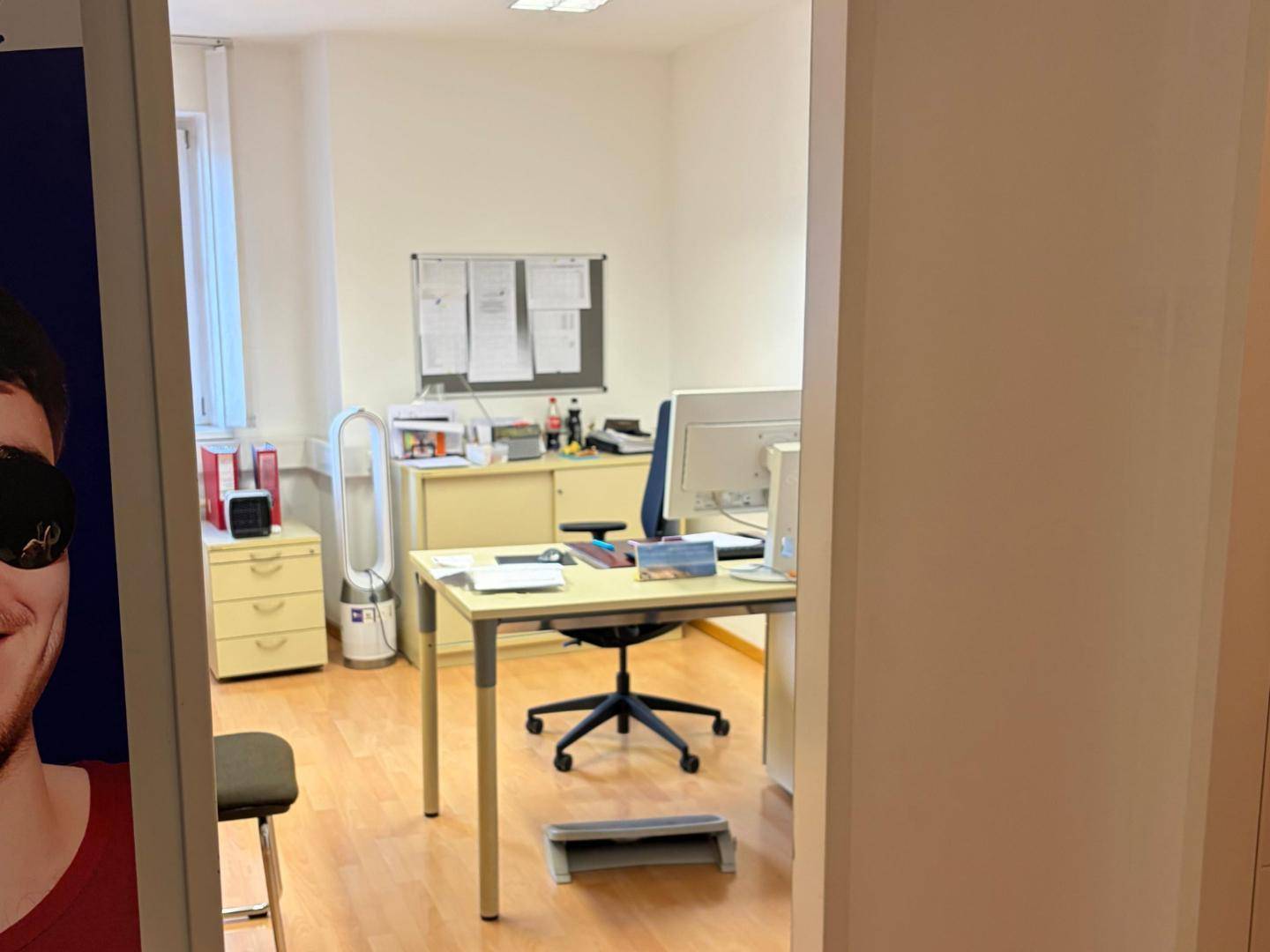 Funktionales Büro mit Schreibtisch, Bürostuhl und Pinnwand, gut beleuchtet.