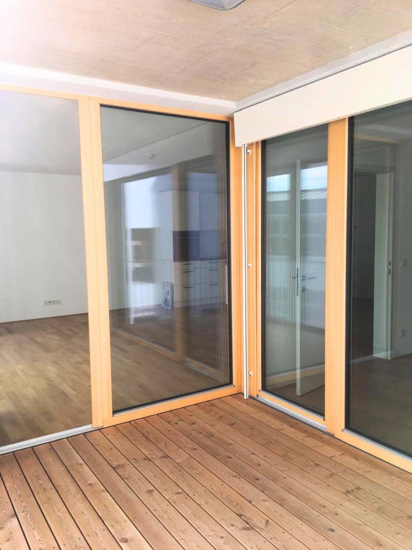 Geräumige Loggia mit Holzboden und großen Glasfronten zum Innenbereich der Wohnung.