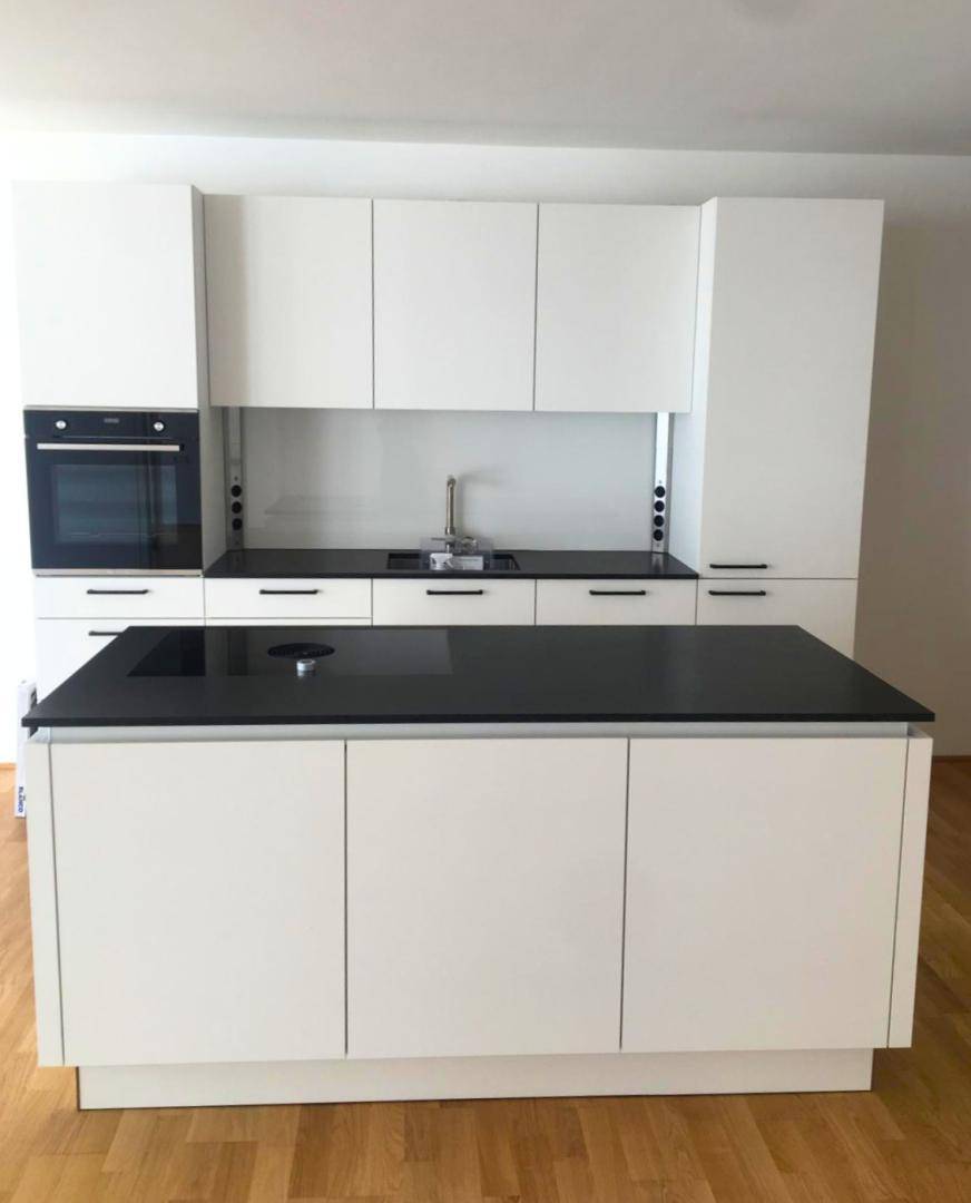 Moderne weiße Einbauküche mit schwarzer Arbeitsplatte, integriertem Backofen und Kochfeld.