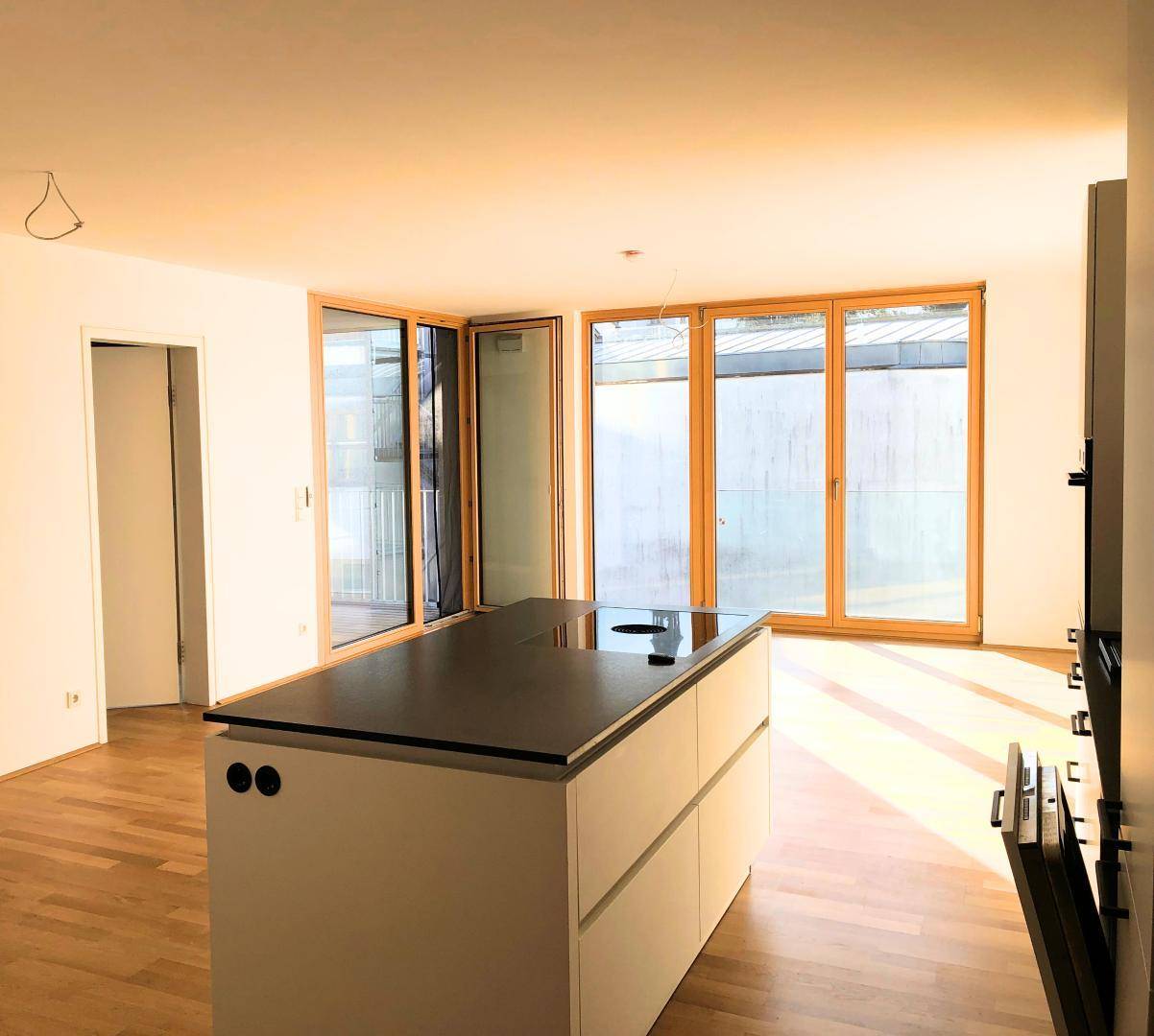 Lichtdurchfluteter Wohnbereich mit Kücheninsel, Parkettboden und Zugang zu einem Außenbereich.