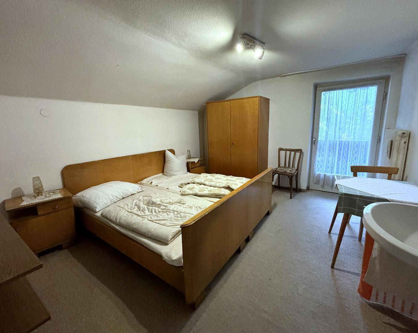 Schlafzimmer mit zwei Einzelbetten, Kleiderschrank und Zugang zu einem Balkon, unter einer Dachschräge.