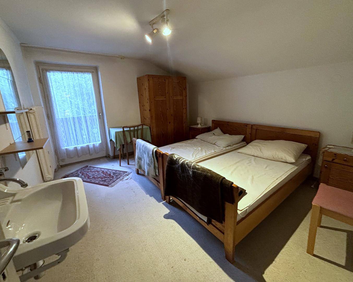 Helles Schlafzimmer mit zwei Einzelbetten, Waschbecken und Zugang nach draußen, unter einer Dachschräge.