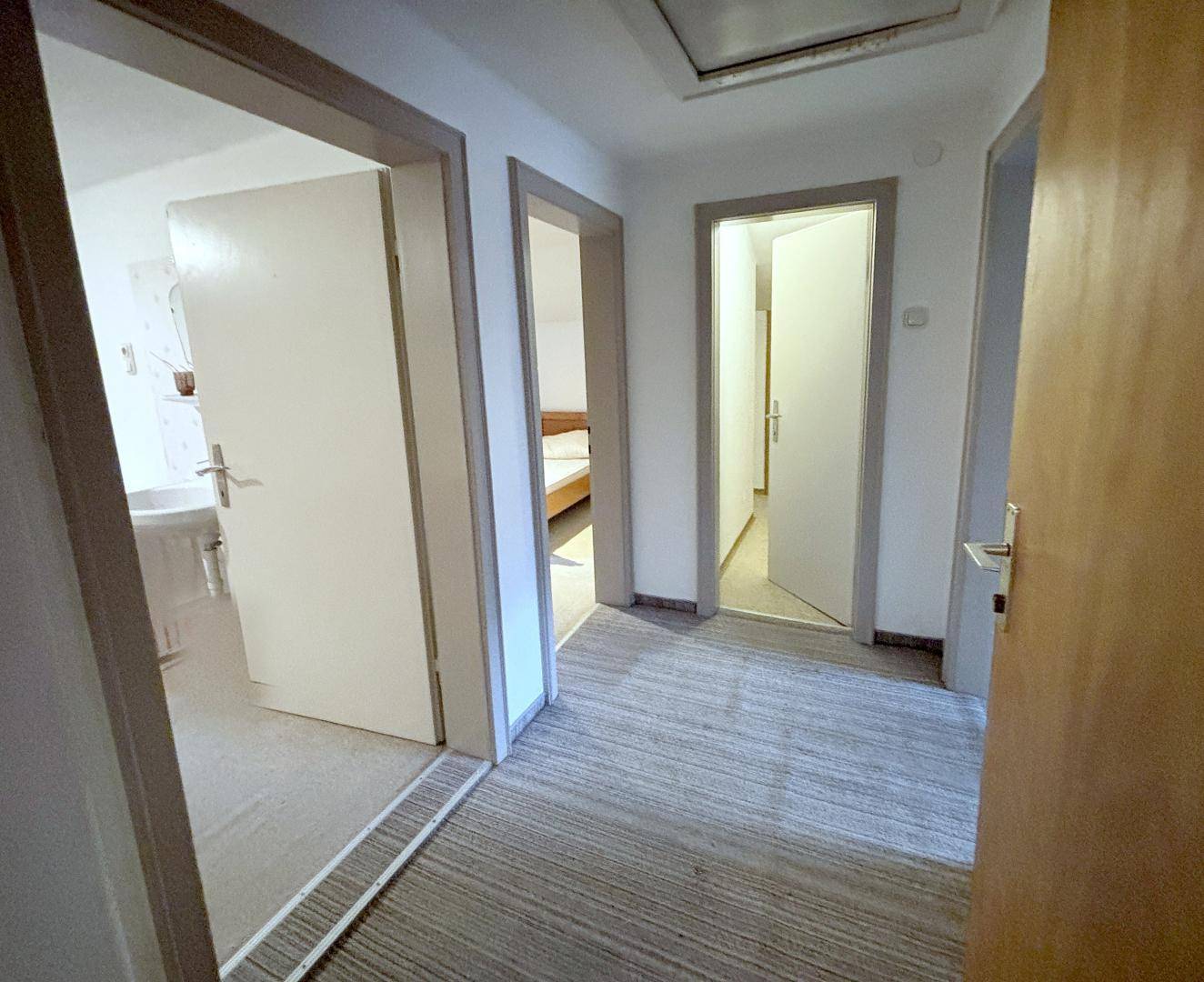 Heller Flur mit mehreren Türen, die zu verschiedenen Zimmern führen, und Teppichboden.