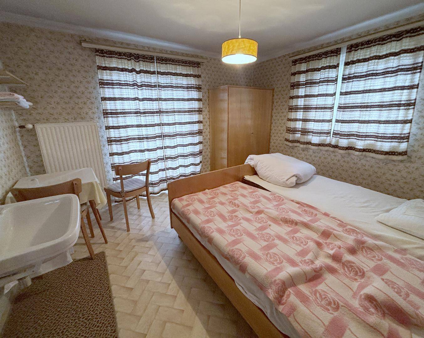 Gemütliches Schlafzimmer mit zwei Einzelbetten, floraler Tapete und einem Waschbecken im Raum.