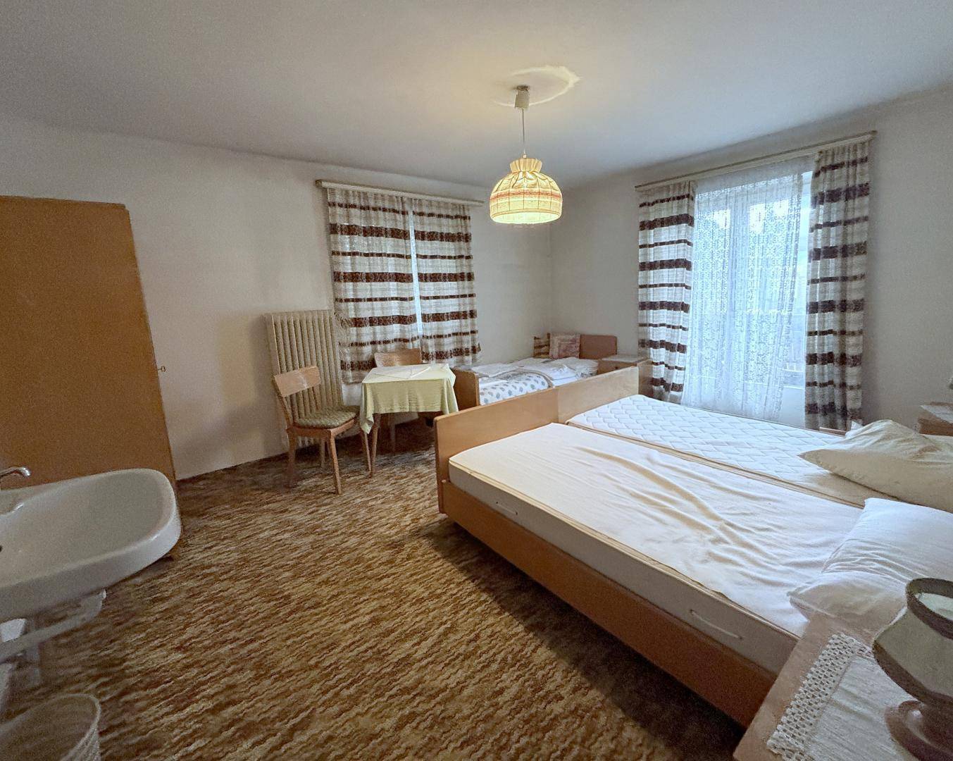Geräumiges Schlafzimmer mit mehreren Einzelbetten, Waschbecken und gemustertem Teppichboden.