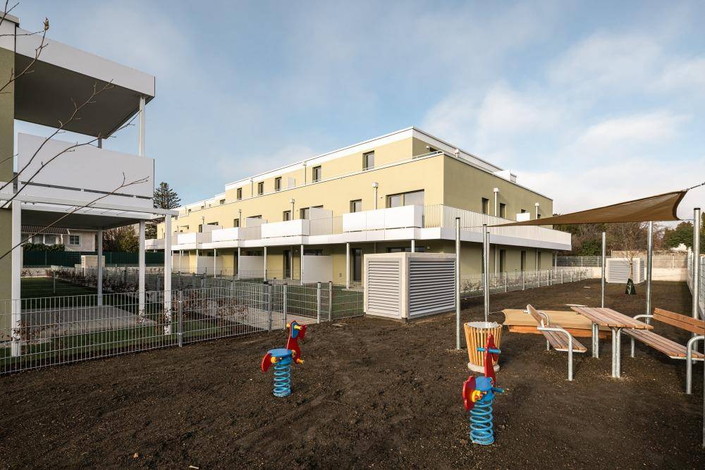 Moderne Wohnanlage mit Spielplatz und Reihenhäusern unter klarem Himmel.