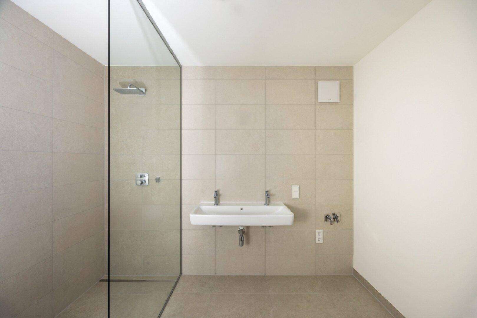 Modernes Badezimmer mit begehbarer Dusche, Doppelwaschbecken und hellen Fliesen an den Wänden.