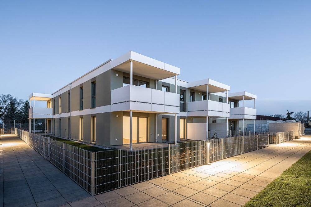 Moderne Reihenhäuser bei Dämmerung mit beleuchteten Terrassen und Gärten.