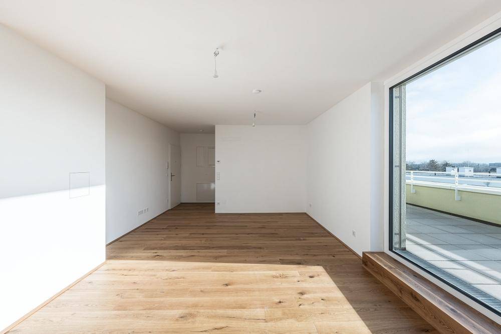 Heller Wohnbereich mit Holzboden und großem Fenster mit Blick auf die Dachterrasse.