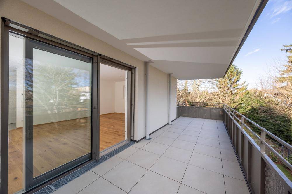 Heller Balkon mit Zugang zu einem Zimmer mit Holzfußboden und Blick ins Grüne.