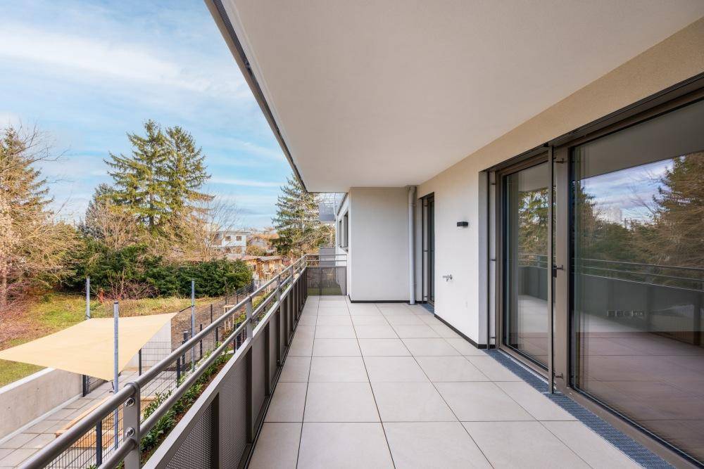 Großer Balkon mit Fliesenboden und Metallgeländer, bietet einen weiten Blick ins Grüne.