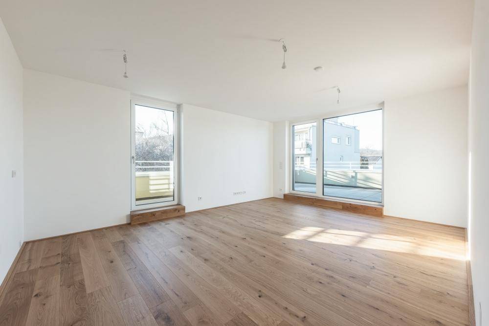 Lichtdurchfluteter Raum mit Holzboden und Zugang zu einem französischen Balkon.
