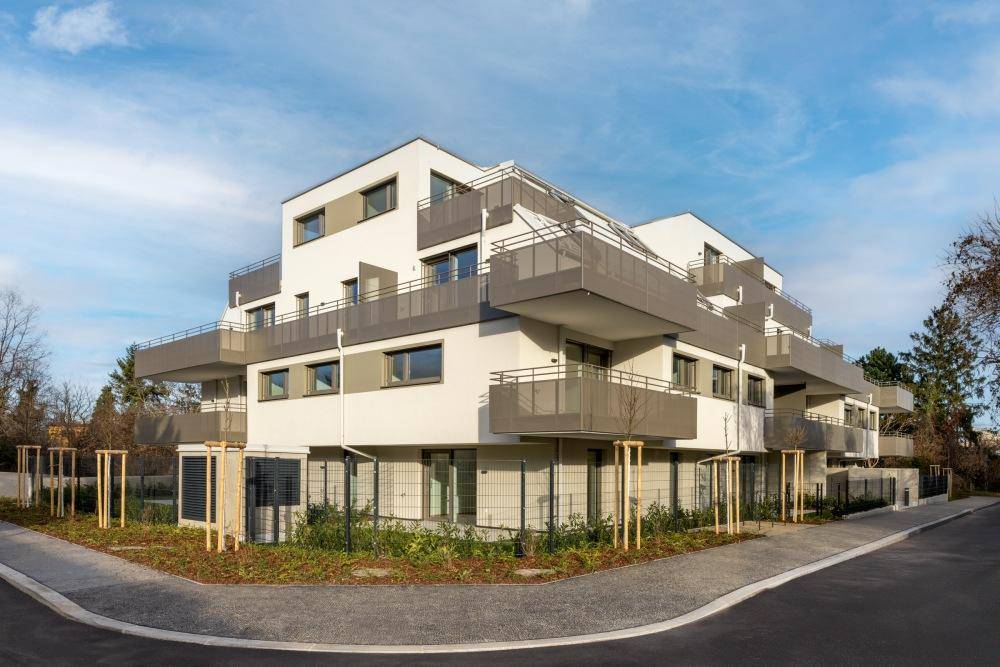 Modernes Mehrfamilienhaus mit zeitgenössischer Architektur, vielen Balkonen und gepflegter Außenanlage.