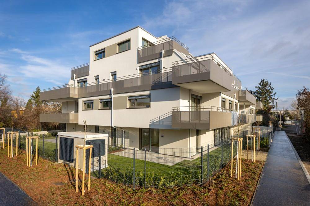 Neubau-Eckansicht mit modernen Balkonen, privaten Gärten und sauberer Außenanlage.