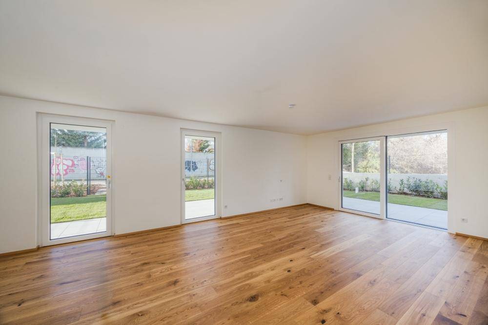Helles Wohnzimmer mit Holzfußboden und mehreren Glastüren, die direkten Zugang zum Garten bieten.