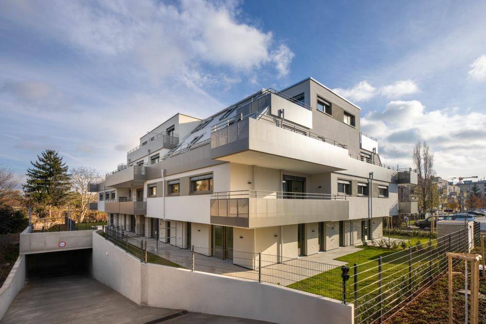 Modernes Wohngebäude mit Tiefgaragenzufahrt, Balkonen und gepflegten Grünflächen im Außenbereich.
