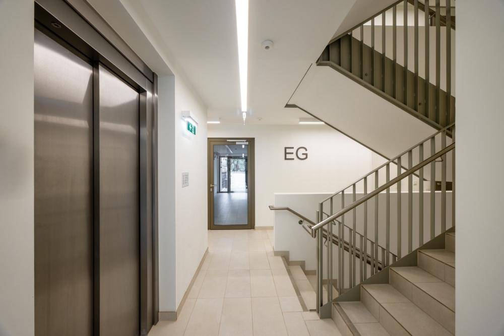 Heller Flur im Erdgeschoss mit modernem Aufzug und Treppenhaus, gut beleuchtet.