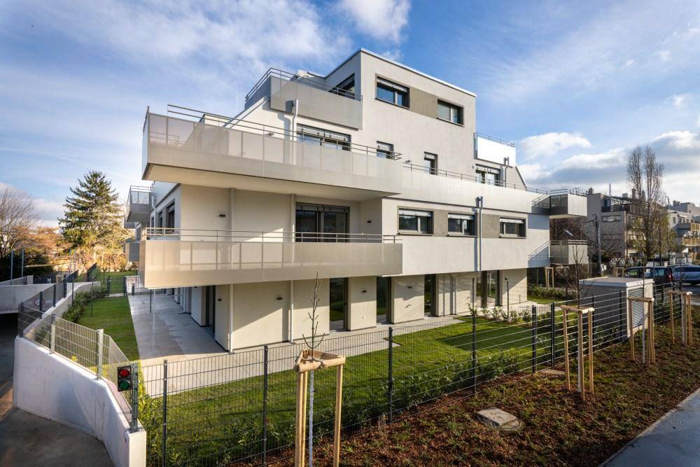 Ansicht des modernen Wohnkomplexes mit Tiefgaragenzugang und umliegenden Grünflächen bei Tageslicht.