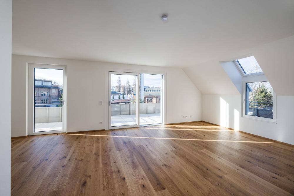 Helles Zimmer mit Holzfußboden, Dachschräge, Dachfenster und Zugang zu einem Balkon.
