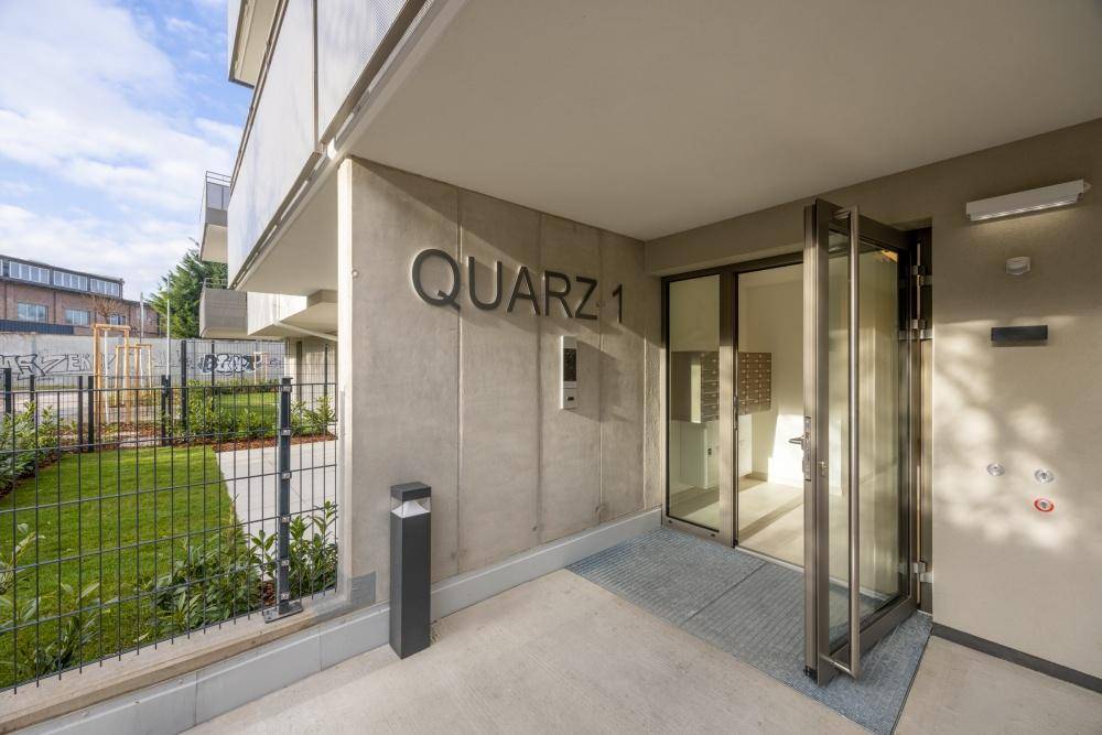 Moderner Eingangsbereich des Gebäudes 'QUARZ 1' mit Glasportal und barrierefreiem Zugang.