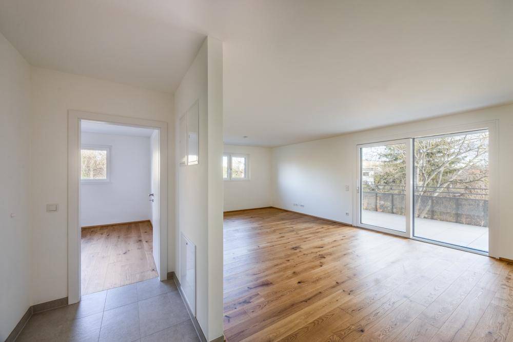 Geräumiges Wohnzimmer mit hellem Holzfußboden und großem Schiebefenster zum Balkon.