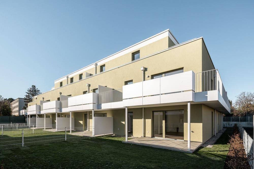 Moderne Reihenhäuser mit Balkonen und Terrassen, umgeben von grünen Rasenflächen.