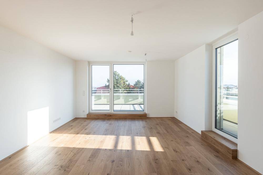 Lichtdurchfluteter Raum mit Holzboden und großen Fenstern, die den Raum hell erscheinen lassen.