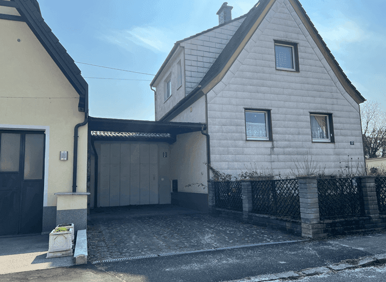 Älteres Einfamilienhaus mit Schieferfassade, Garage und Stellplatz im Freien.