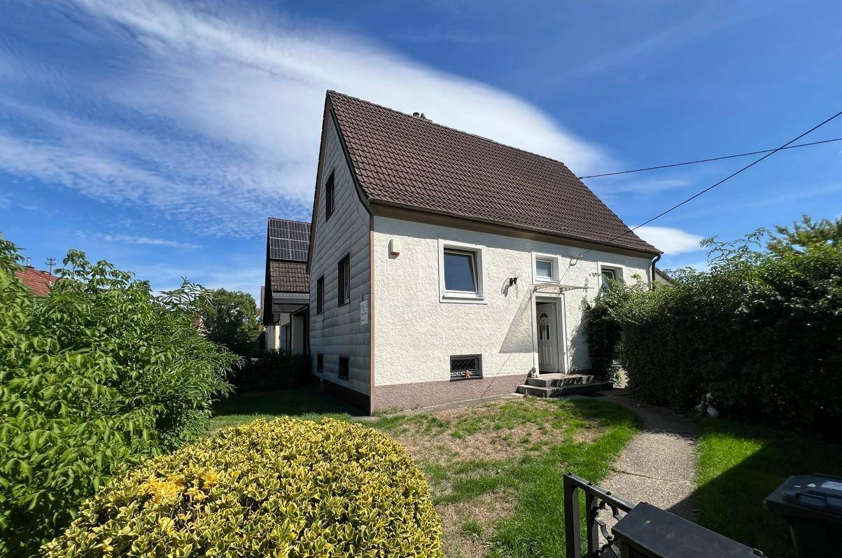 Einfamilienhaus mit Satteldach, heller Fassade und gepflegtem Vorgarten unter strahlend blauem Himmel.
