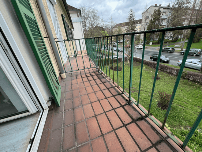 Balkon mit Terrakottafliesen, grünem Geländer und Blick auf die Straße.