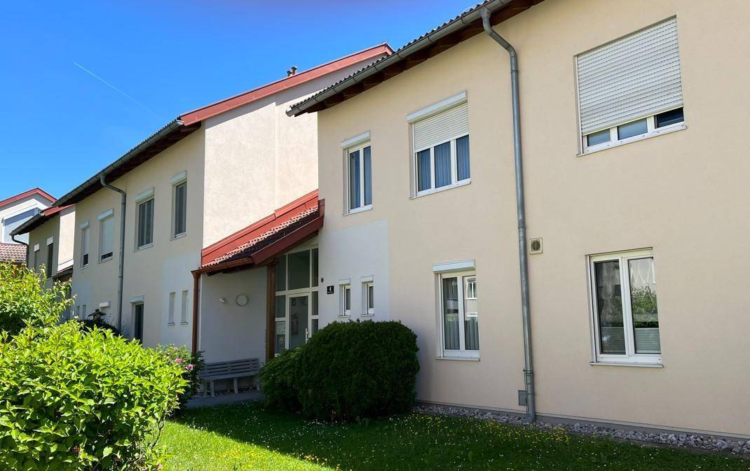 Fassade eines Mehrfamilienhauses in hellem Beige mit weißen Fenstern und Rollläden.