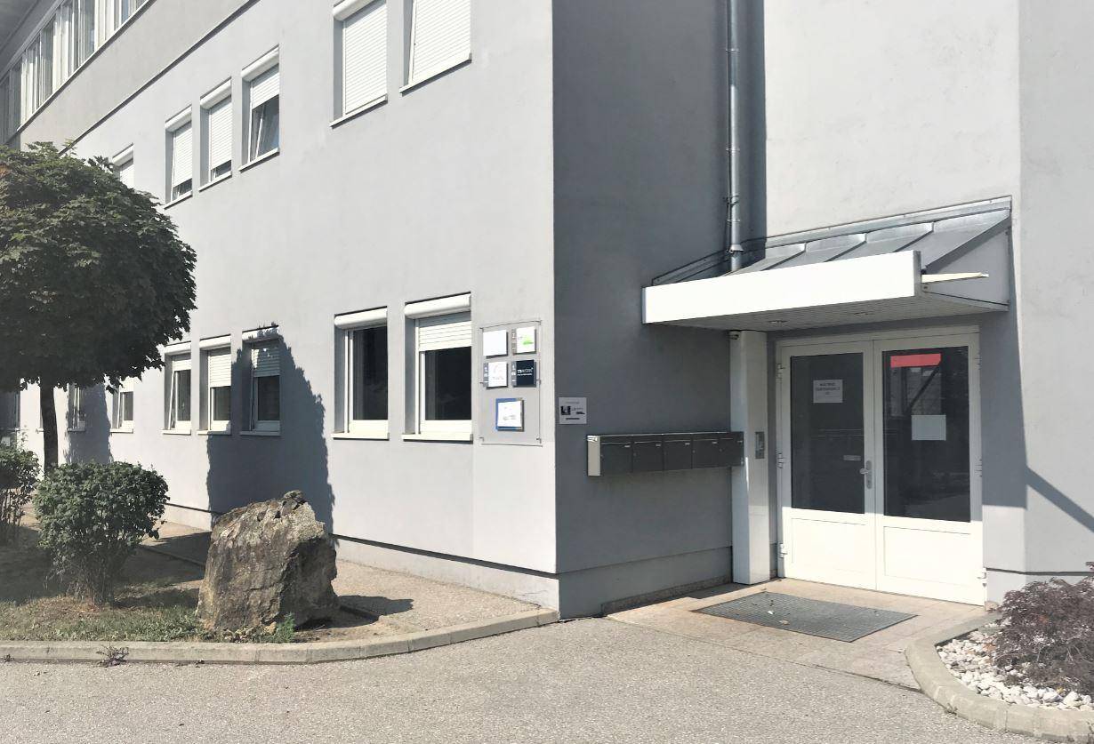 Eingangsbereich des Geschäftsgebäudes mit Vordach und Briefkästen an der grauen Fassade.